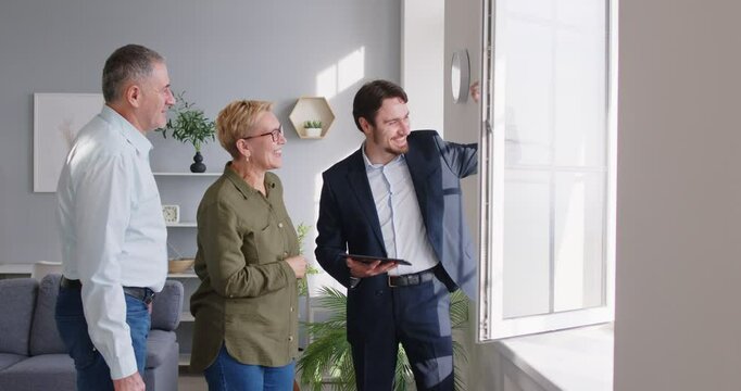 Realtor showing house to a mature senior happy couple looking at the view from the window. Professional real estate agent showing new apartment. Real estate market concept. 4k video.