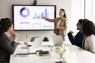 Positive young Asian project leader woman presenting marketing report to workgroup, pointing hand...