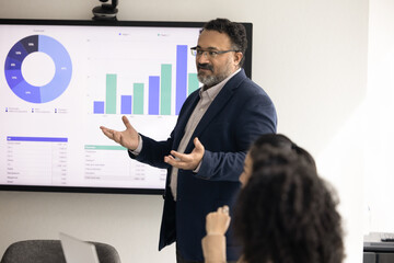 Mature Indian company CEO presenting sales growth analytics to group of employees, colleagues,...