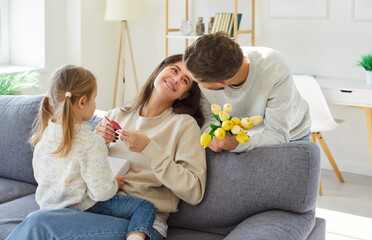 In cozy living room at home, father and his little daughter happily wish their mother happy...