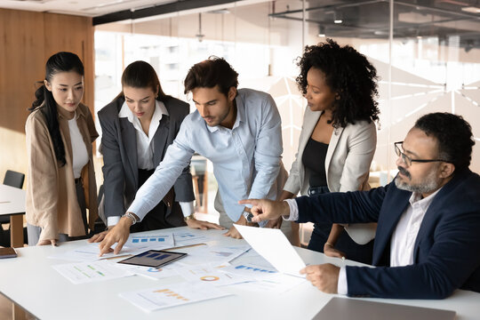 Multiethnic creative business group working on sales reports together, analyzing financial marketing data, discussing financial project strategy, enjoying teamwork, company diversity