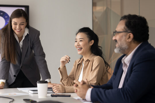 Cheerful diverse business colleagues meeting at table offline, talking, discussing sales reports presentation, creative teamwork approach, ideas for project, talking, laughing, enjoying communication - Powered by Adobe