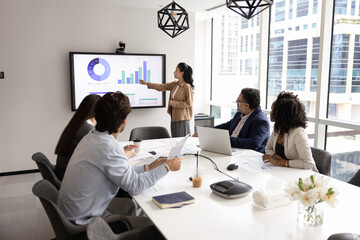 Young Asian business leader woman presenting financial sales reports to diverse team of colleagues,...