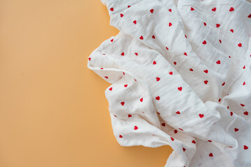 Flat lay of white muslin fabric with red hearts on a pastel peach background