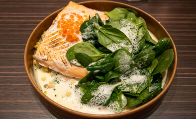 Portion of grilled wild scottish salmon served with green spinach and white cream sauce and red caviar