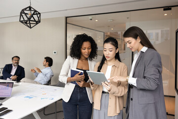 Multiethnic business team of young female colleagues analyzing online project content. Young Asian...