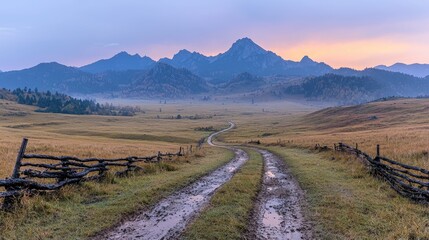 Obraz premium Muddy dirt road winds through a grassy valley towards distant mountains under a colorful twilight sky.