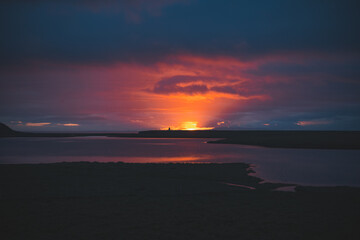 Stunning sunset on the Snaefellsnes peninsula, Iceland, with vibrant pink and purple hues reflecting perfectly on the calm water. A serene and breathtaking view near Grundarfjordur