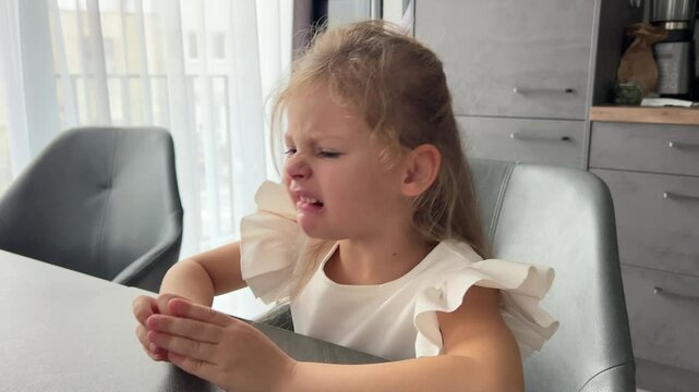 Little girl sitting at a table coughs very hard and tries to cough it up, choking or due to illness
