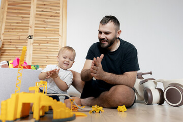 Happy Father and funny son playing with yellow toy construction set at home