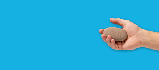 Fototapeta premium Man hand holding stone on blue background with copy space.