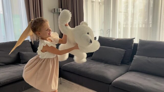Little girl dancing with big plush polar bear at home in living room