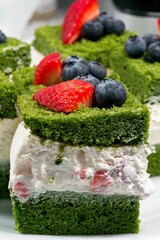 A green layer of sponge cake topped with whipped cream, blueberries, and strawberries.