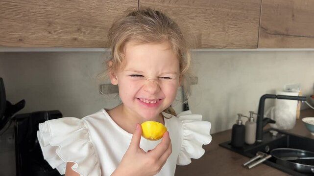 Little girl wincing as she tastes lemon sitting in kitchen