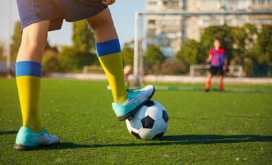 A young soccer player is balancing a soccer ball with their foot on a green field, wearing yellow...