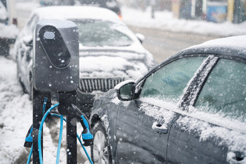 Electric car charging station on a background of snow covered winter cars.