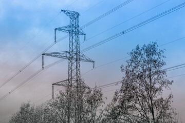 Fototapeta premium A high-voltage electricity pylon with power lines stretching across the sky during dusk. The silhouette contrasts with the gradient hues of blue and orange in the background.