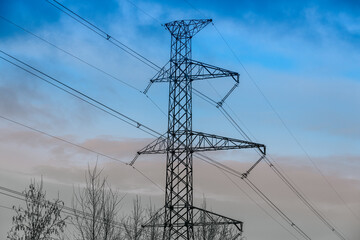 A high-voltage electricity pylon with power lines stretching across the sky during dusk. The...