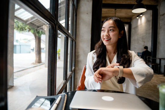 Young asian businesswoman checking the time on her smartwatch while waiting for a business meeting in a modern cafe - Powered by Adobe