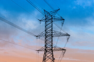 A high-voltage electricity pylon with power lines stretching across the sky during dusk. The...