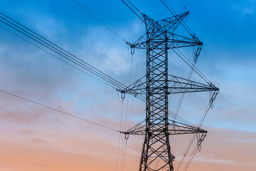A high-voltage electricity pylon with power lines stretching across the sky during dusk. The...
