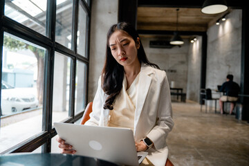 Young asian businesswoman with concerned expression working on laptop in a cafe