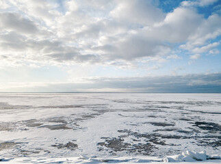 Bright sun shining over over the frozen sea. Winter seascape: clouds above the huge lake covered with ice and snow.