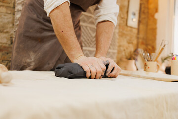 Artisan in apron pressing black clay in pottery studio