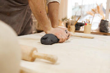 Cropped view of artisan pressing clay near rolling pin in pottery studio