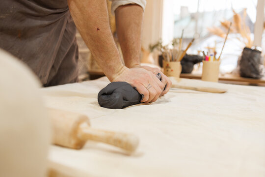 Cropped view of artisan pressing clay near rolling pin in pottery studio