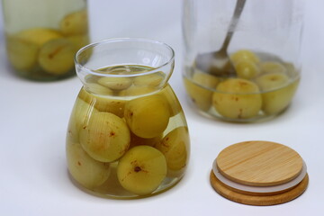 Brine pickled Indian gooseberries in glass bottle, surrounded by fresh gooseberries