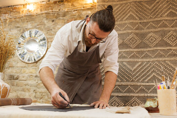 Artisan cutting black clay while working in pottery studio