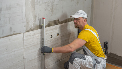 Tiling with large format tiles. A tiler measuring the verticality of the tile by a spirit level.