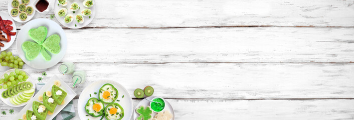 St Patricks Day breakfast or brunch corner border against a white wood banner background. Variety of green and shamrock themed pancakes, toasts, eggs, fruits and meats. Overhead view. Copy space. © Jenifoto
