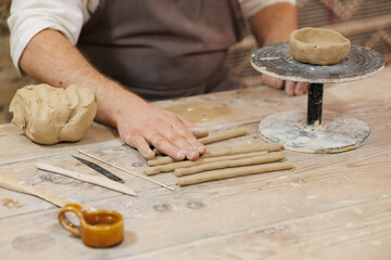 Partial view of potter rolling clay near wheel and tools in studio