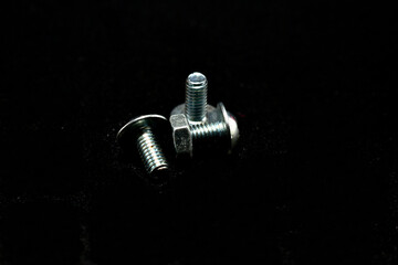Short bolts with nuts lie on the table on a black background.