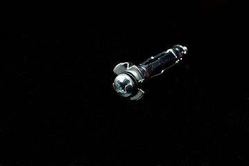 One anchor bolt for fastening parts on plasterboard lies on a black background.