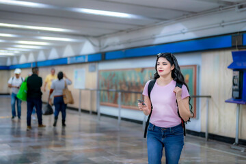 Confident young Latina woman with wavy hair, pink t-shirt, jeans, and a backpack prepares to enter...