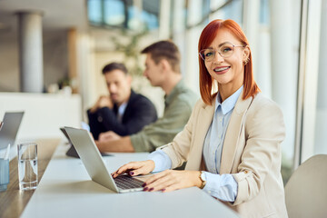 Professional Woman Smiling in Office Environment with Colleagues in Background