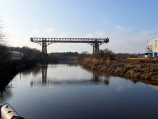 Historic industrial bridge spanning over a tranquil river landscape.