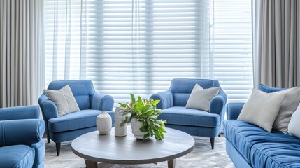 Cozy living room with blue sofas and easy chairs, window blinds, and sheer white curtains.