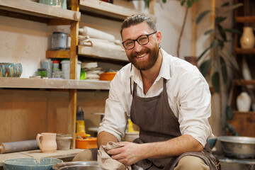 Cheerful potter holding towel near pottery wheel in studio