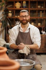 Smiling artisan cleaning hands near pottery wheel in workshop