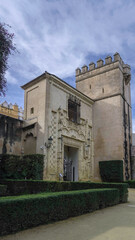 Obraz premium A historic stone building with an ornate entrance and a fortified tower stands against the blue sky. Trimmed hedges frame the structure, enhancing its medieval charm.