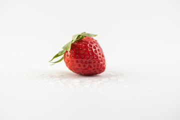 on white photo background lies one ripe strawberry in the center of the background drops of water healthy vitamins seasonal summer fruit vitamin C green strawberry tail like a crown