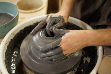Part of craftsman shaping clay on pottery wheel in studio