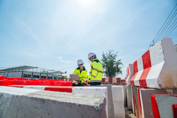 Two engineers wearing high visibility jackets discuss construction progress near concrete...