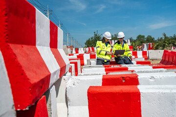 Two engineers wearing high visibility jackets discuss construction progress near concrete...