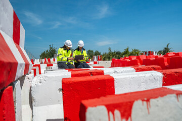 Two engineers wearing high visibility jackets discuss construction progress near concrete...