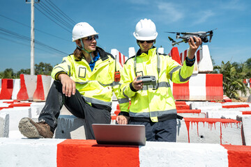 Two engineers in reflective jackets and helmets sit amidst red-and white barricades at a...